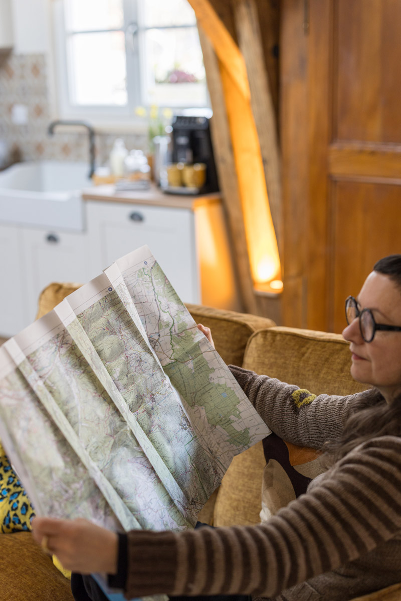 Photo d'une personne consultant une carte IGN pour préparer une randonnée, depuis le canapé de l'espace salon du gîte « À toi l'Aviateur ! » à Wattwiller - photo Marie Soehnlen