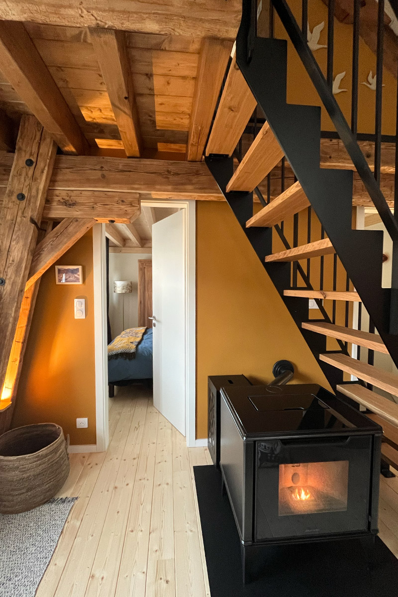 Photo du poêle à pellets, de la porte de la chambre Fleurs et de l'escalier menant à la chambre Cabane du gîte « À toi l'Aviateur ! » à Wattwiller